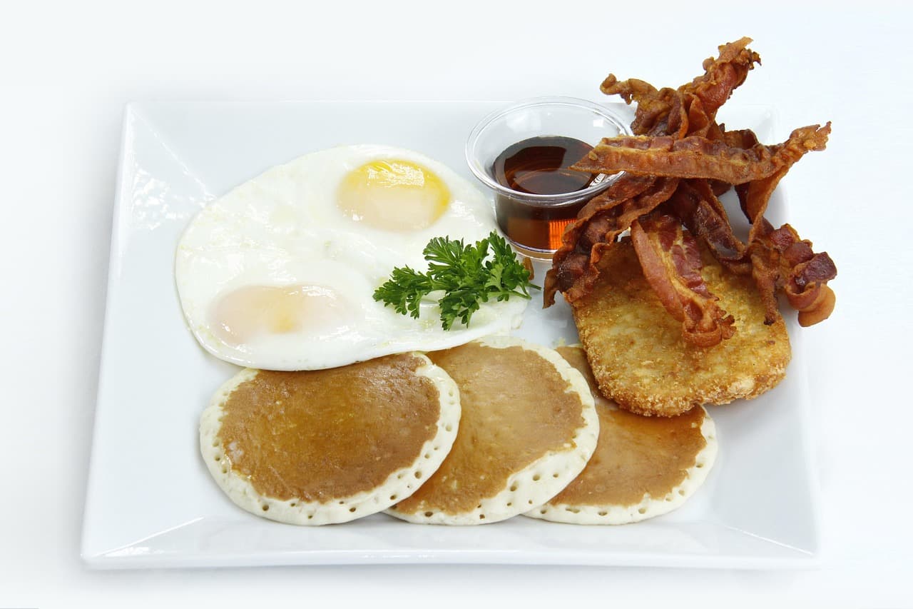 Fried eggs, crisp bacon, pancakes and golden hash browns on a white plate