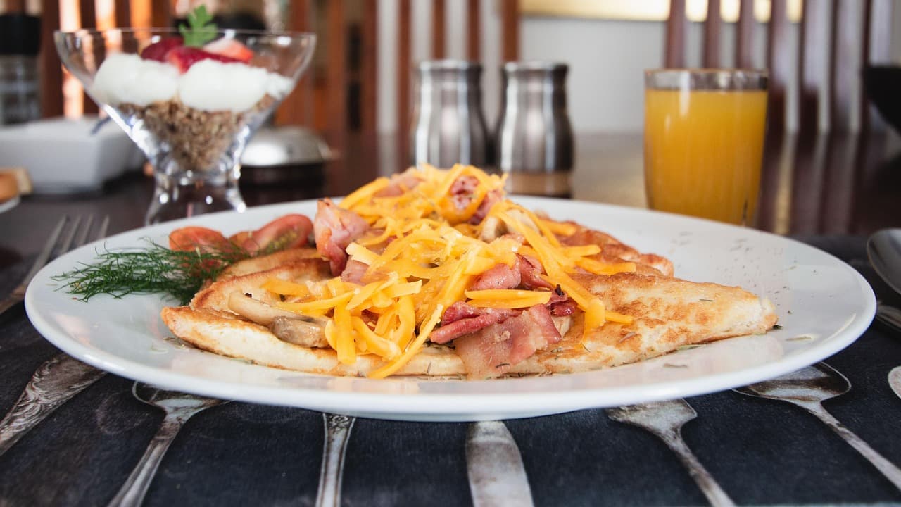 A folded crepe topped with melted cheese and bacon, orange juice behind