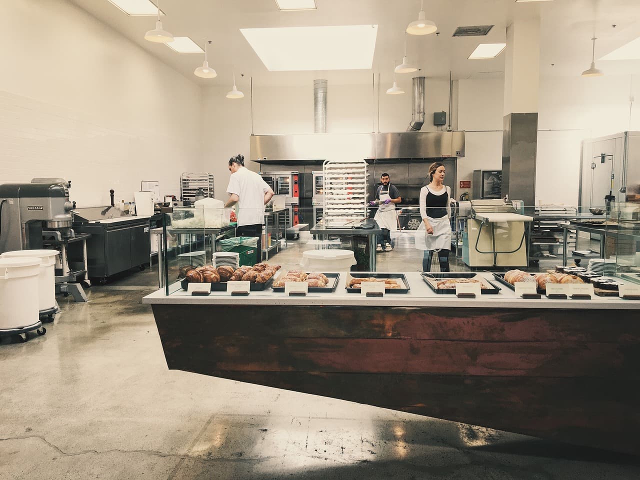 An open kitchen behind a counter of fresh bakes, cooks at work